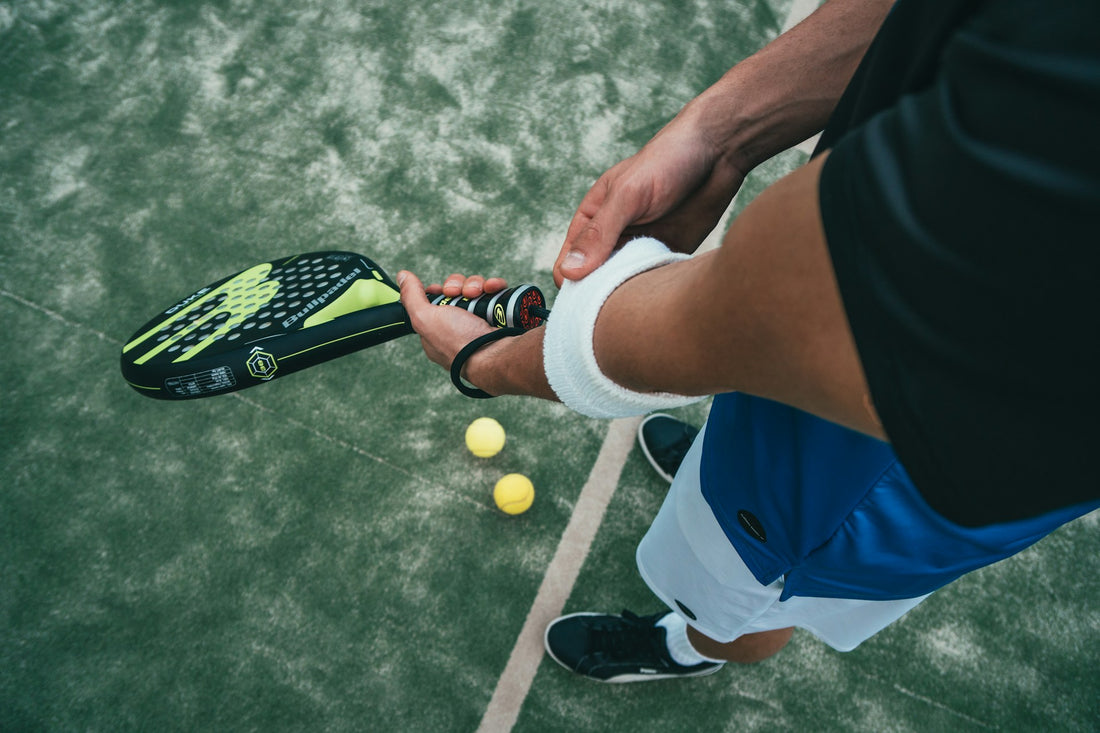 A man stands on the edge of a padel court, holding a racket and wearing a sweat band.